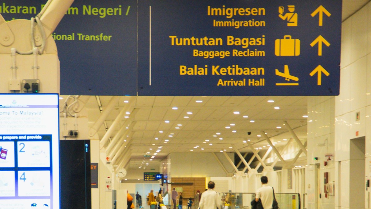 Immigration and baggage reclaim signs in Malay and English at an airport